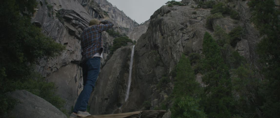 A man takes a picture of a waterfall from a log