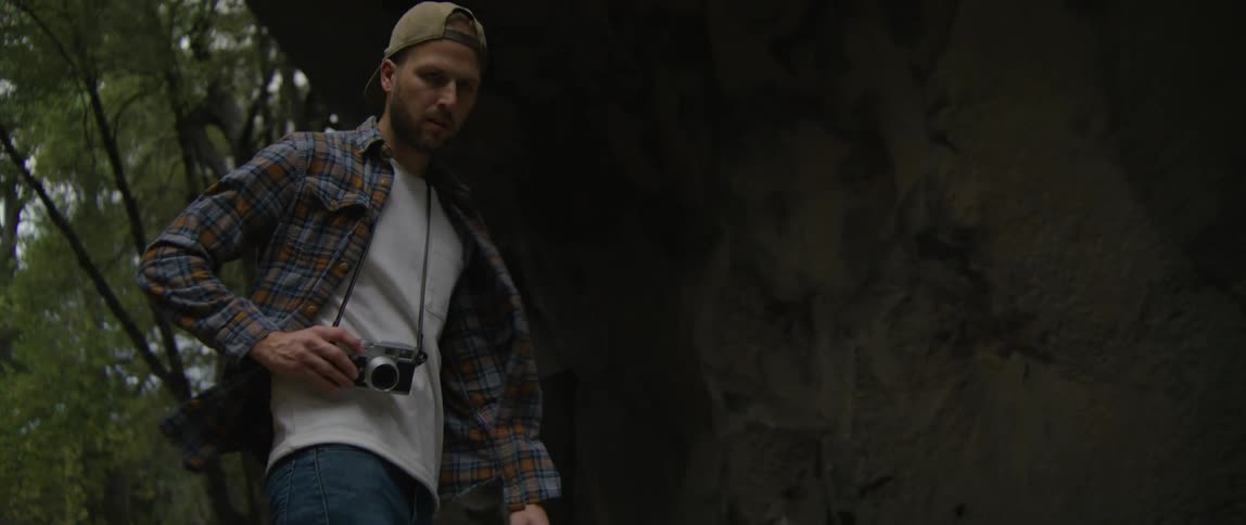 A man carrying a camera while walking outdoors carefully watches his step over uneven terrain
