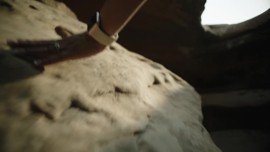 A person with a ring and wristwatch rubbing their hand on a cave wall with the sky and clouds in the background
