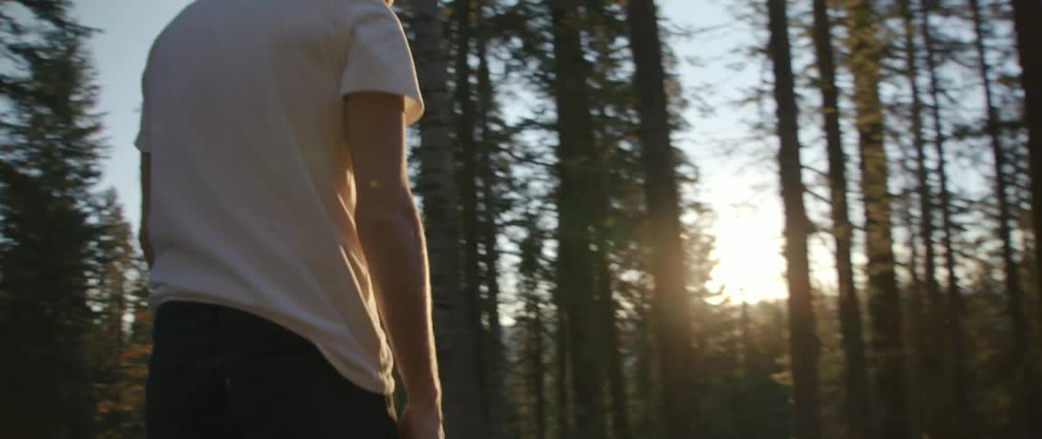 Man riding a skateboard on a rural road through the forest at sunset