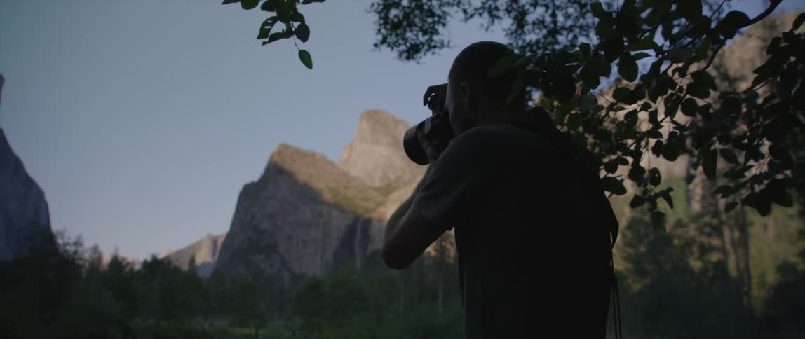 Male photographer taking photos of forest and mountains is silhouetted against the blue sky
