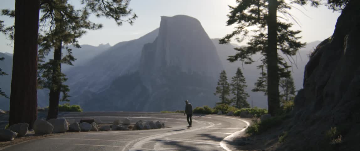 A person is riding a skateboard on a winding road with mountains in the distance