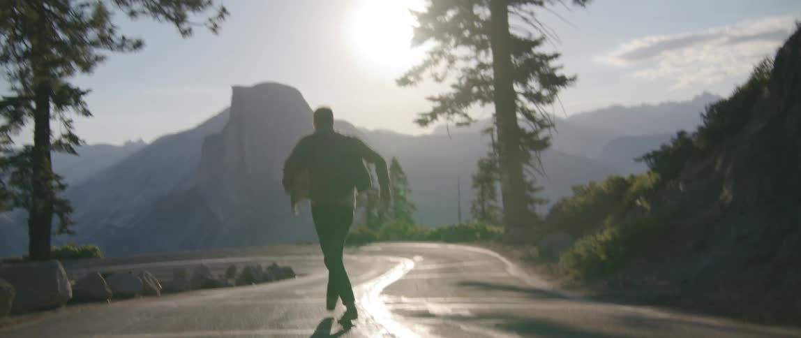 A man running along the middle of a roadway through the mountains jumps with excitement