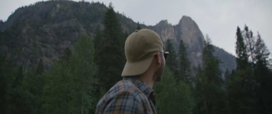 A man is walking in the forest near some peaks in a mountain range