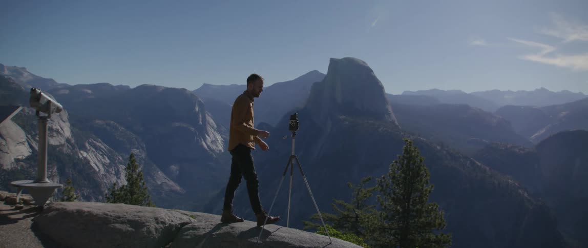 A man walking up to a camera to take photos of a canyon