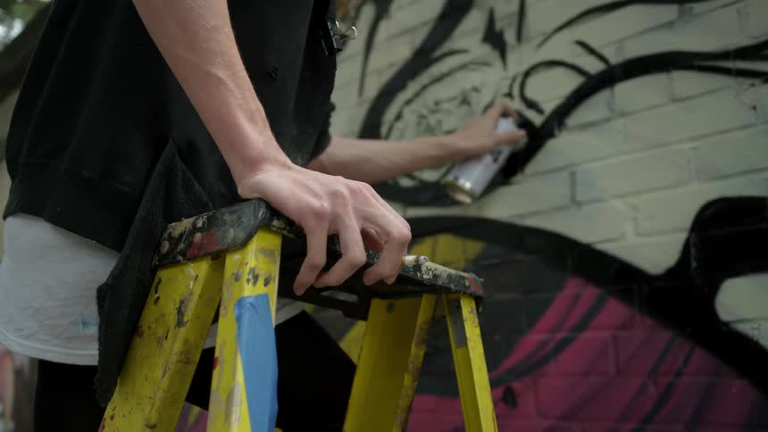 A person spray paints from a ladder