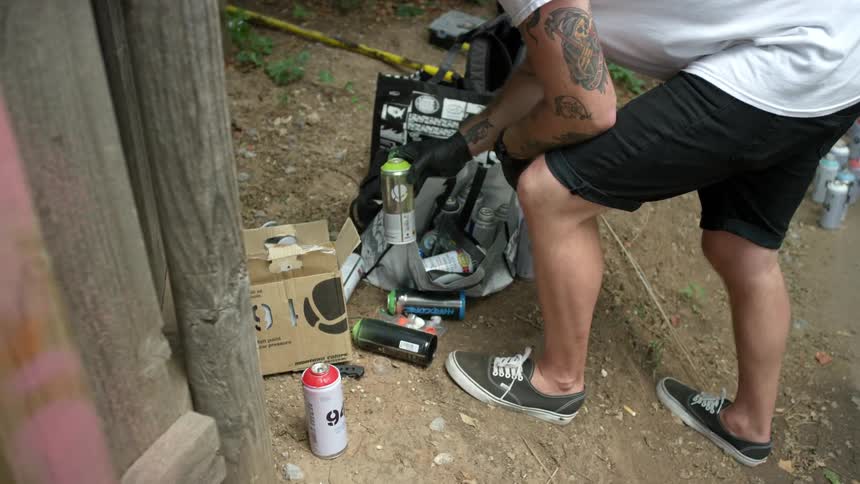 A man removes cans of spray paint from a bag and places them on the ground