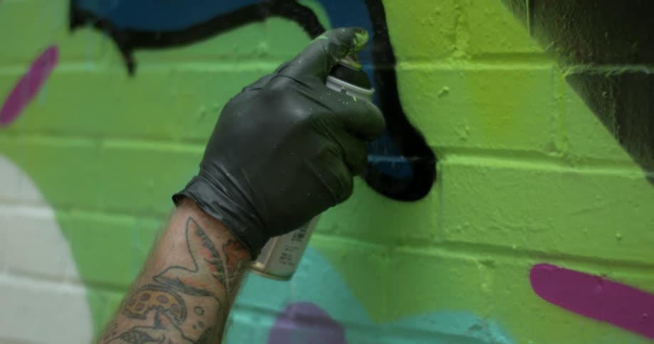 A graffiti artist wearing a rubber glove paints on a brick wall