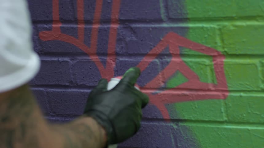 A man spray painting street art on a brick wall