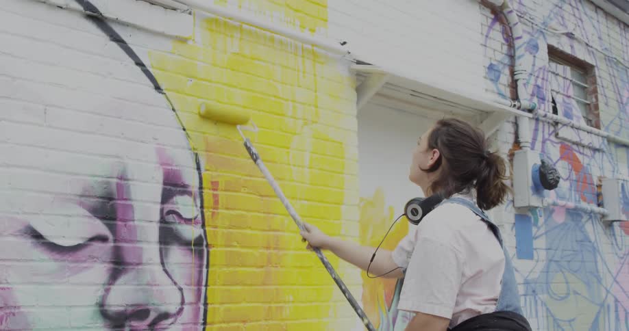 A woman paints a brick wall with yellow paint