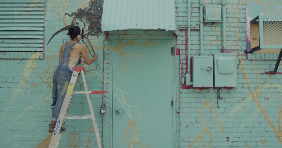 A person is on a ladder painting a brick wall