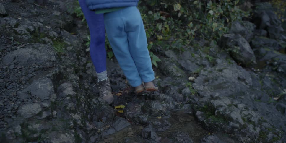 A woman helps a kid jump over a brook