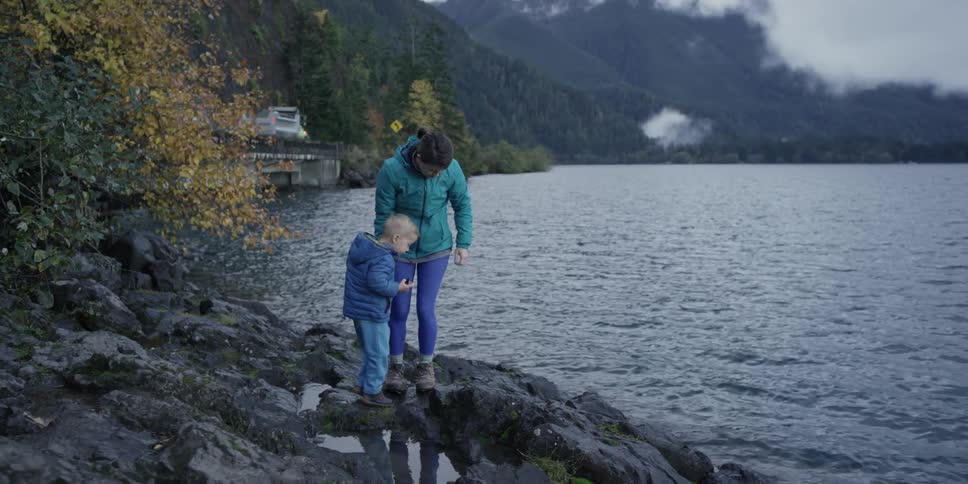 A woman helps a child walk over rocks towards the water