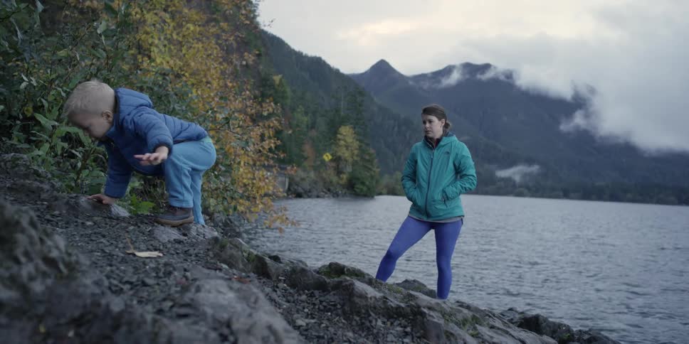A woman watches as her son climbs rocks near the water