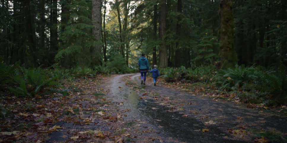 A woman and child walk down a wet forest path
