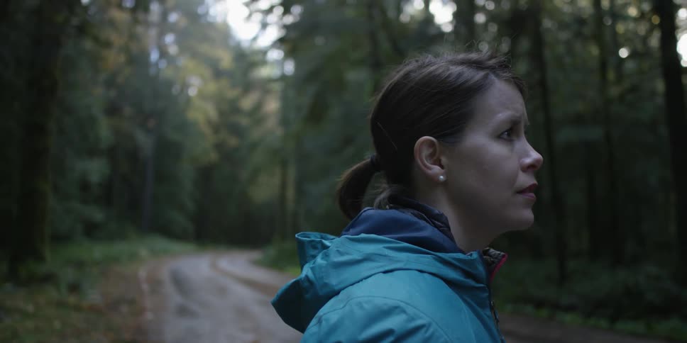 A woman turns on a small trail in the woods looking around