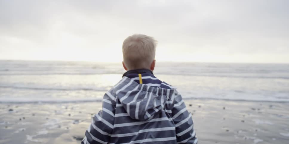A young boy throws a rock toward the sea