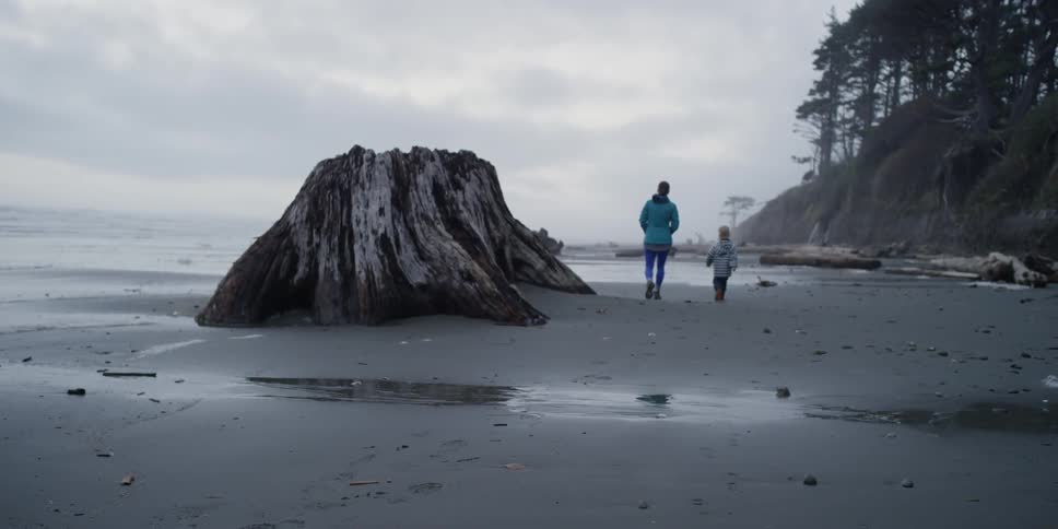 A woman and a young boy walk along a beach on an overcast day