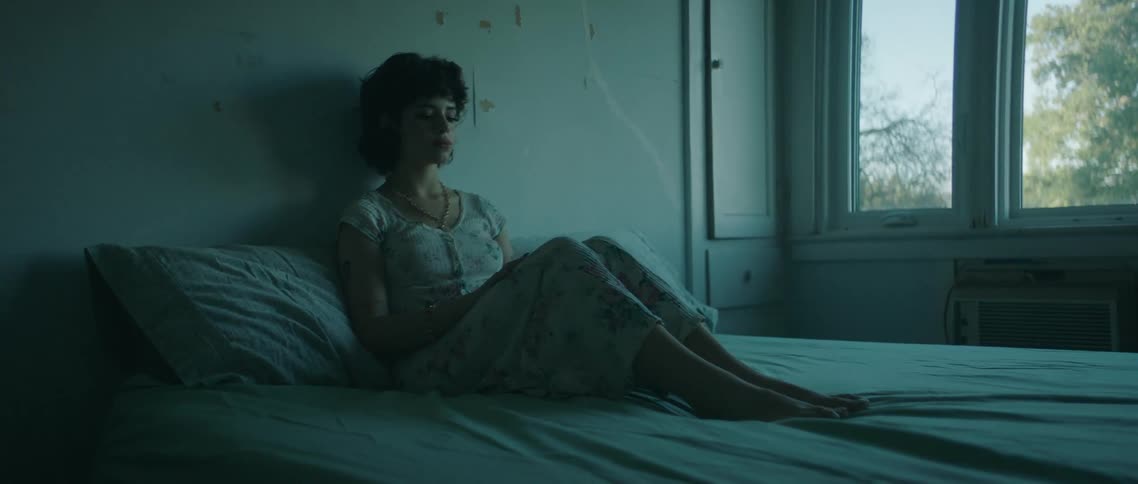 Woman sits on bed reclining with knees bent