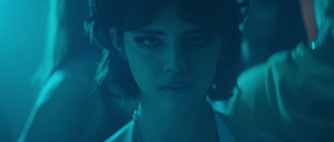A young woman standing with her eyes closed on a dance floor in a night club slowly opens her eyes to gaze into the camera