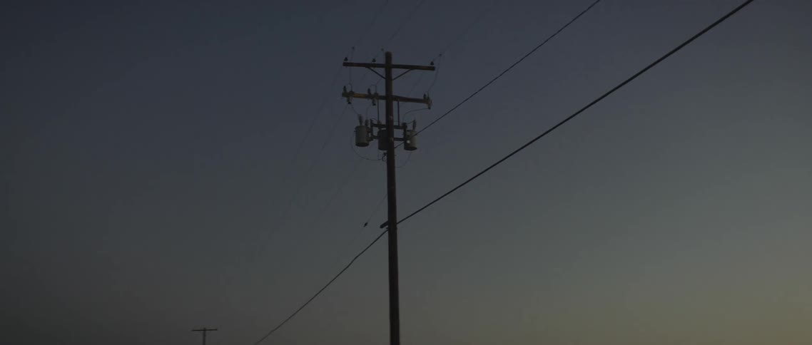 A telephone pole is seen against a dimly lit sky as it supports a number of wires