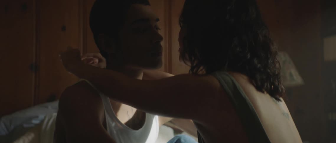 A young man and woman sit on the bed together while lovingly looking into each others eyes