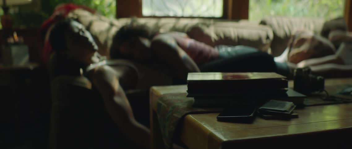 Woman sleeps on man as they cuddle on couch and he thinks about mobile phone