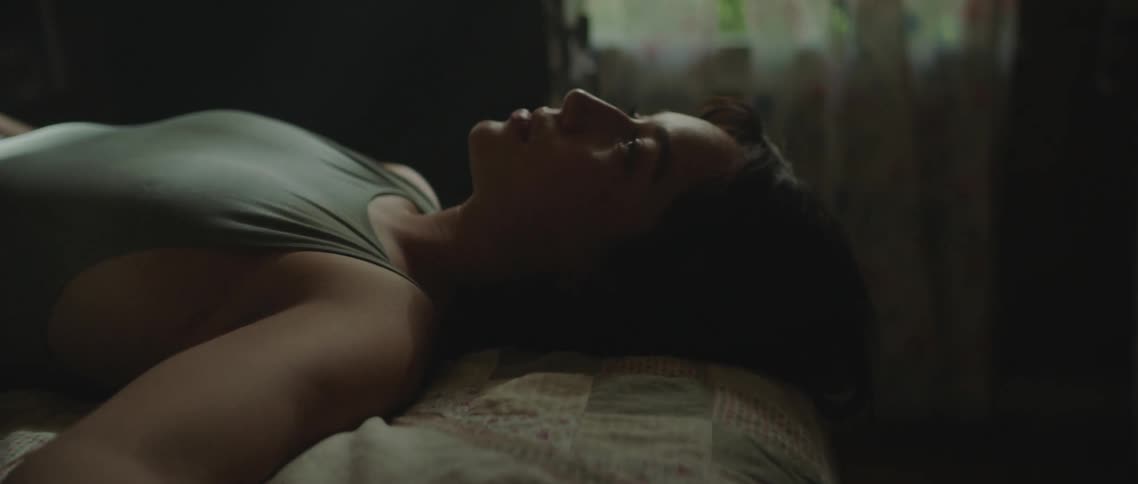 A young woman poses for the camera while laying on her back atop a bed