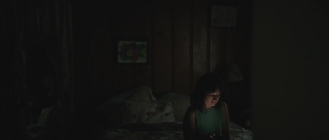 Young woman sitting on the bed looking at her phone in a dark bedroom