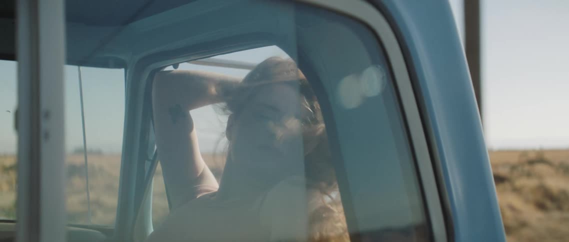A teenage girl holds her hair back as she rides in a truck and leans her head out the window