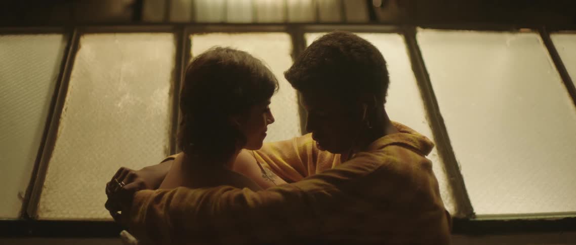 A young man and woman sit together on a rooftop while lovingly embracing each other