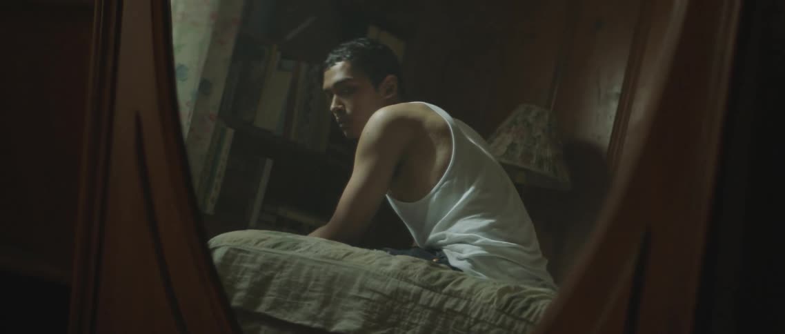 A man is showing sitting on a bed as he looks back at the camera