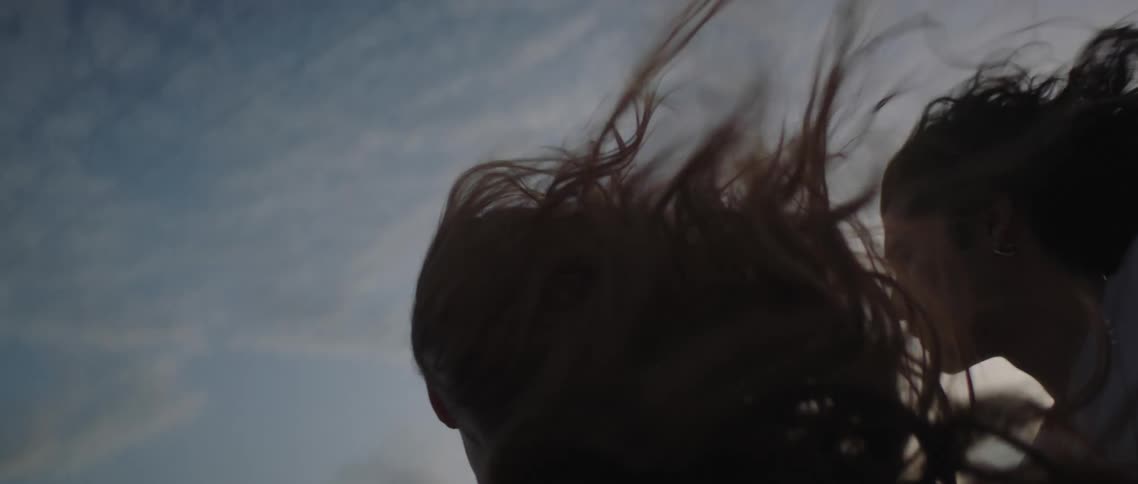 Wind blows hair wildly as man and woman travel under cloudy sky