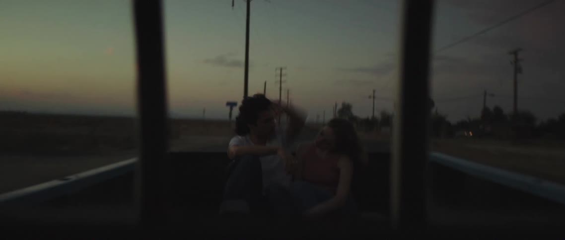 A young couple sit close together as they ride in the back of a pickup truck just as the sun has set