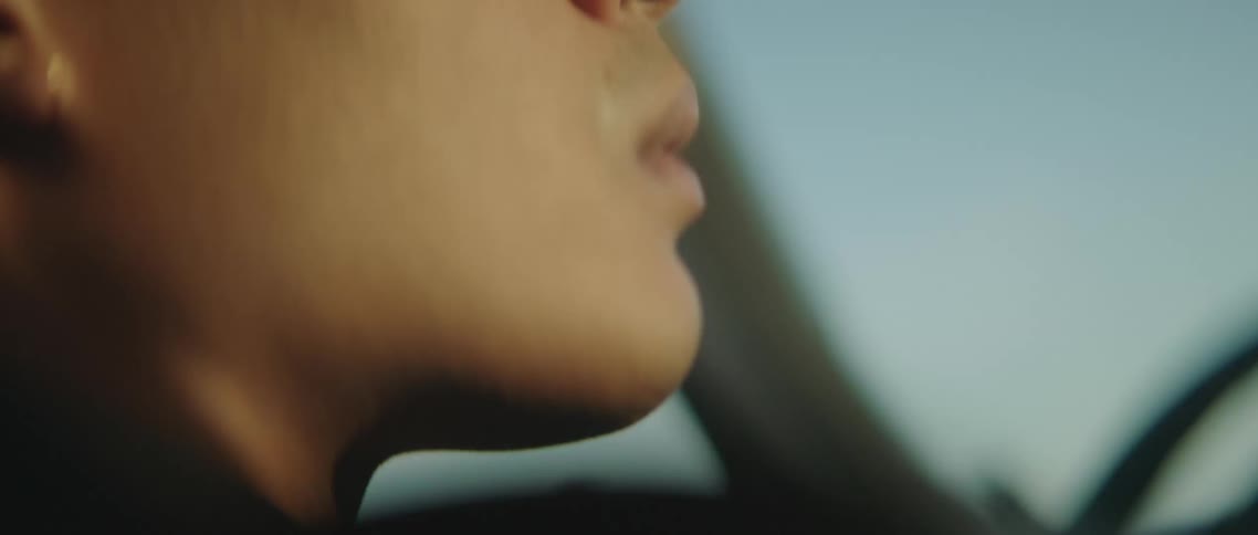 Man blinks slowly as he sits in front seat of car under a blue sky
