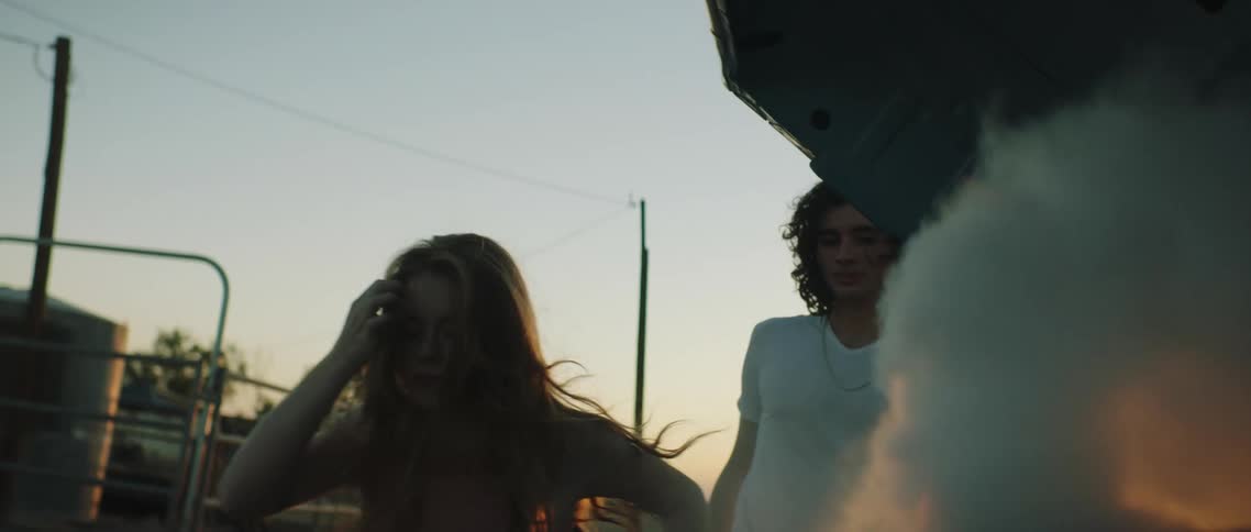 A man and woman standing next to a car that is smoking