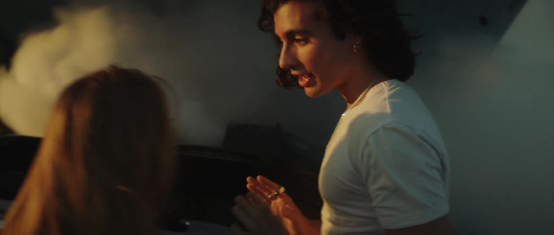 A young man and woman argue while smoke billows from the engine of a nearby car