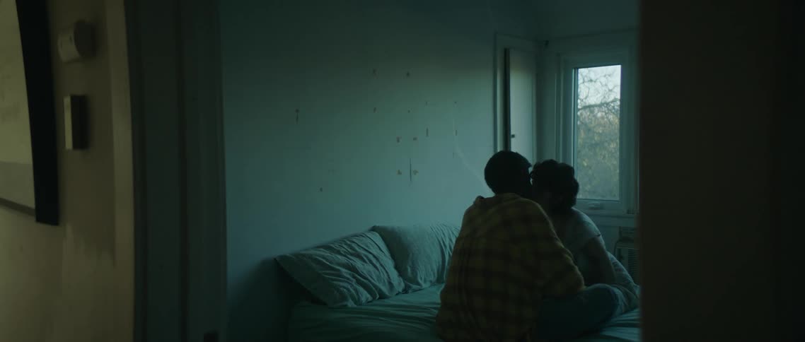 Young couple sitting in bed kissing inside a dimly lit bedroom in the morning