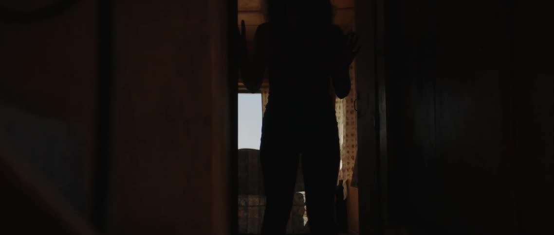 Young blonde woman walking out of a dimly lit house into the birght sunlit exterior