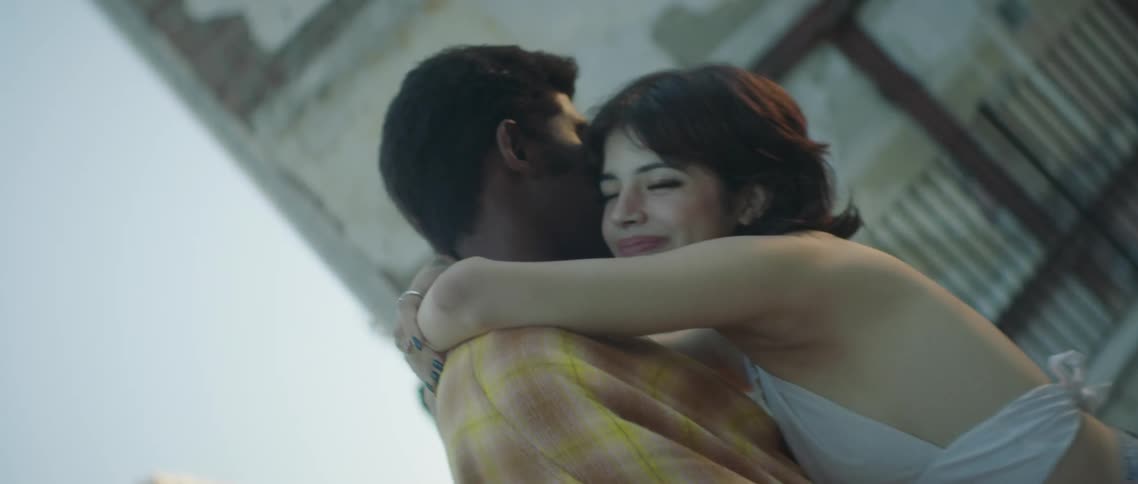 A man and a woman on a rooftop hugging with buildings the sky and clouds in the background