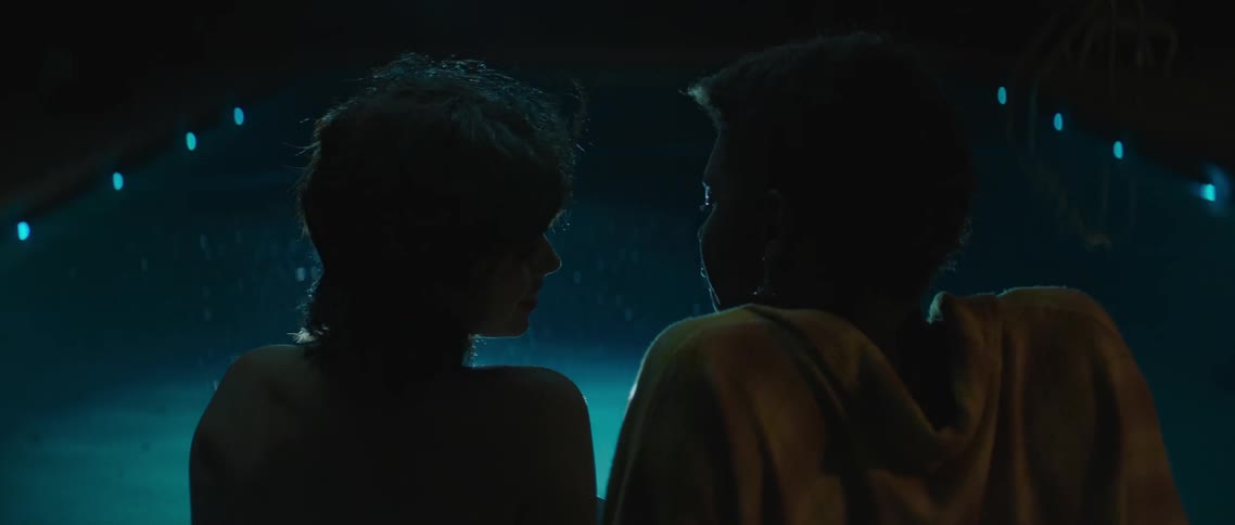 Silhouette of a young couple sitting in front of the reflecting lights on a pool at night