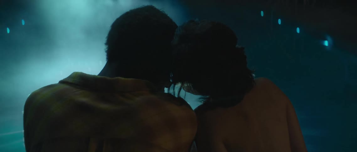 Couple sit together near pool at night leaning to rub noses and cuddle
