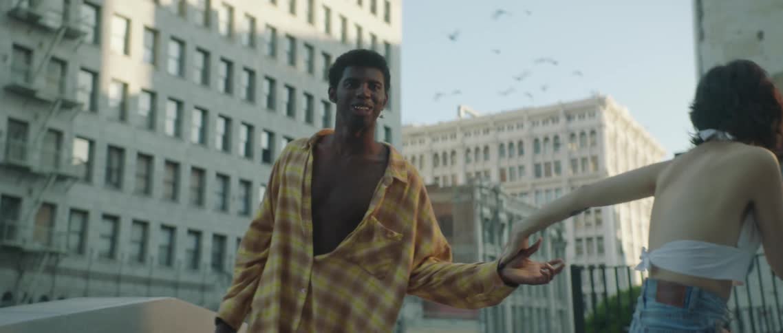 Couple holding hands on rooftop in city laughs after being startled by passing flock of birds