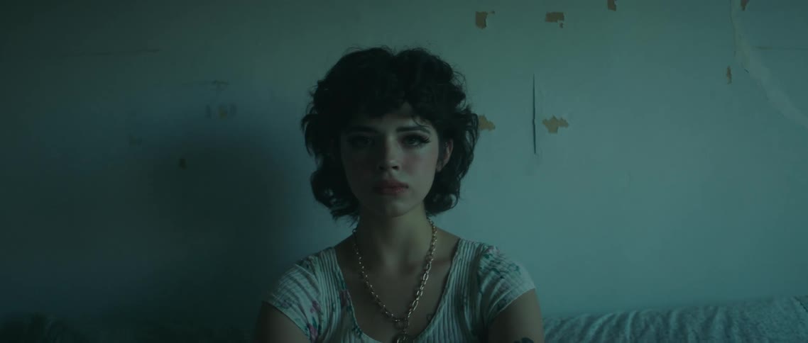 A teenage girl sits on a bed and stares off in to space