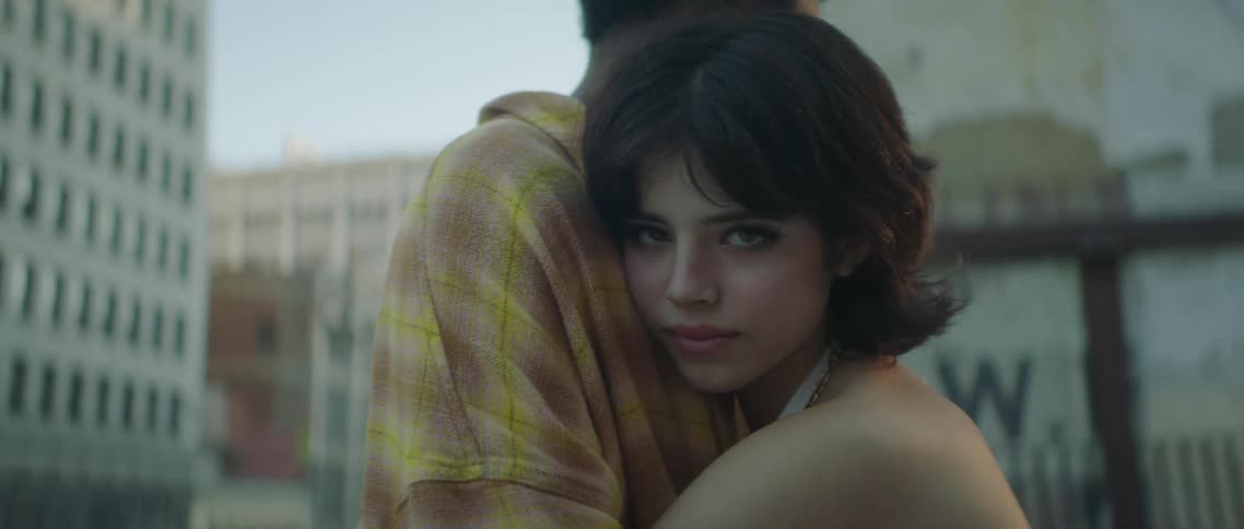 A woman hugs her boyfriend and rests her head on his chest while posing as they stand downtown