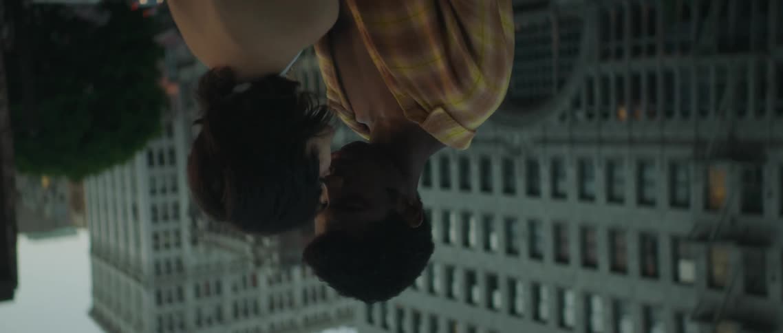 A young man and woman kiss on a rooftop in a metropolis during the day