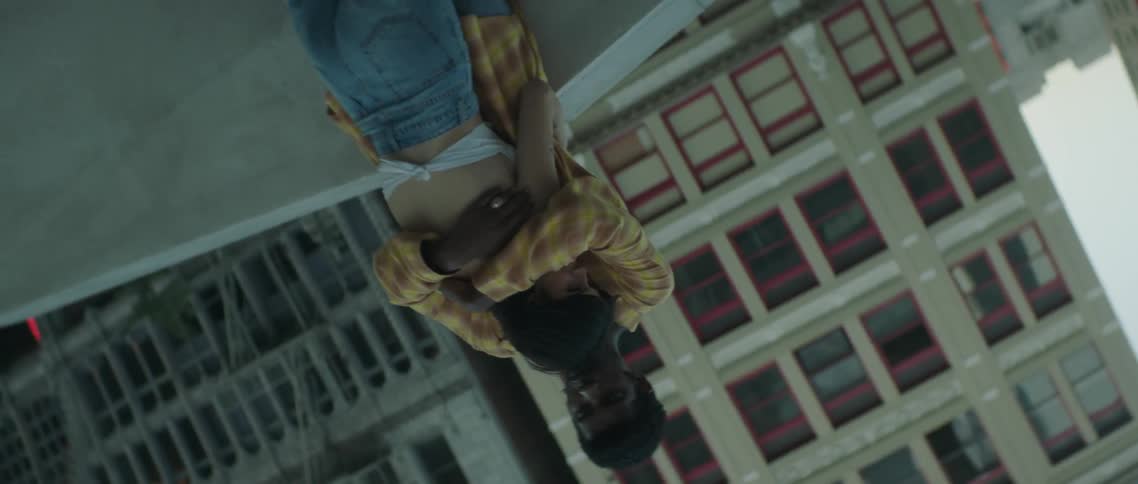 A young man holds his female companion close to him as they stand on a rooftop