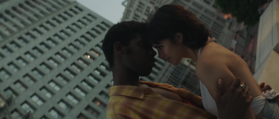 Couple stand together gazing into each others eyes pressing foreheads on rooftop over city street