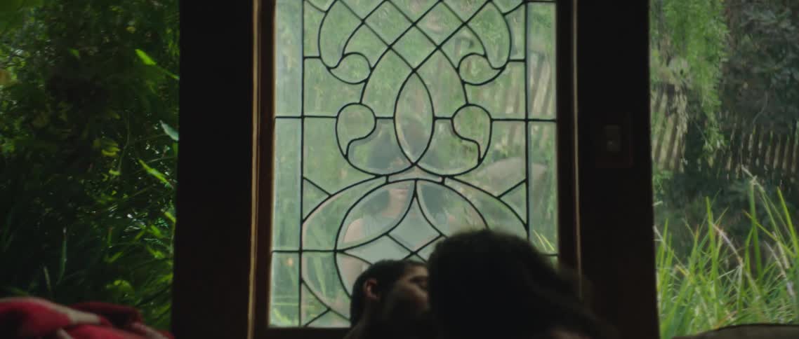 A couple sitting on sofa kisses while another woman looks at that them through window and is visibly upset