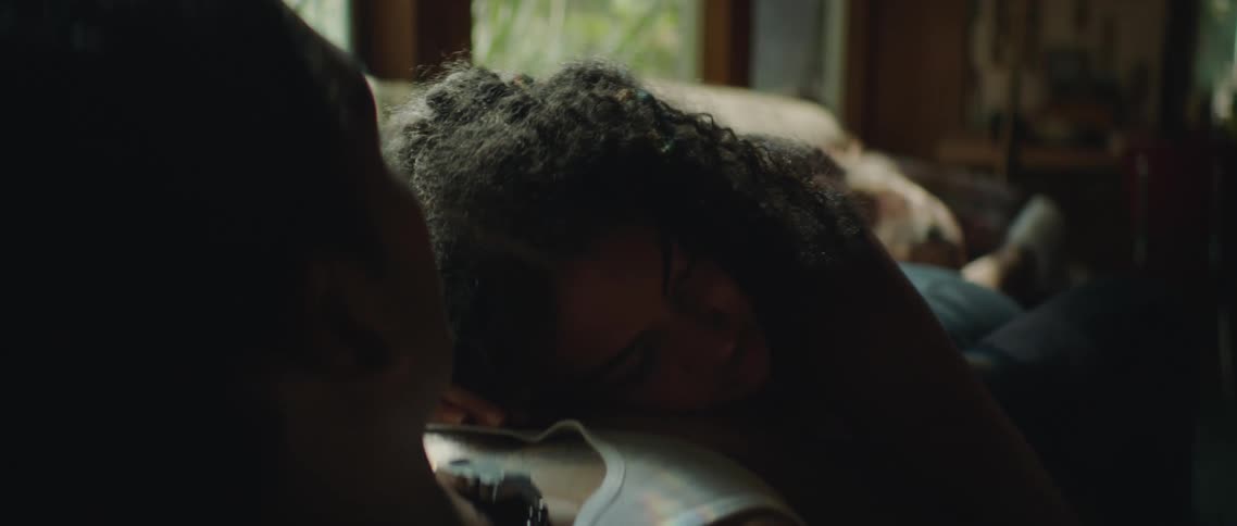 Woman lies on mans chest as they live together on couch while mobile phone on coffee table lights up